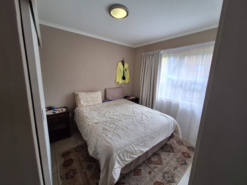 A functional bedroom featuring tiled flooring, a built-in cupboard, and a large window allowing natural light into the space.