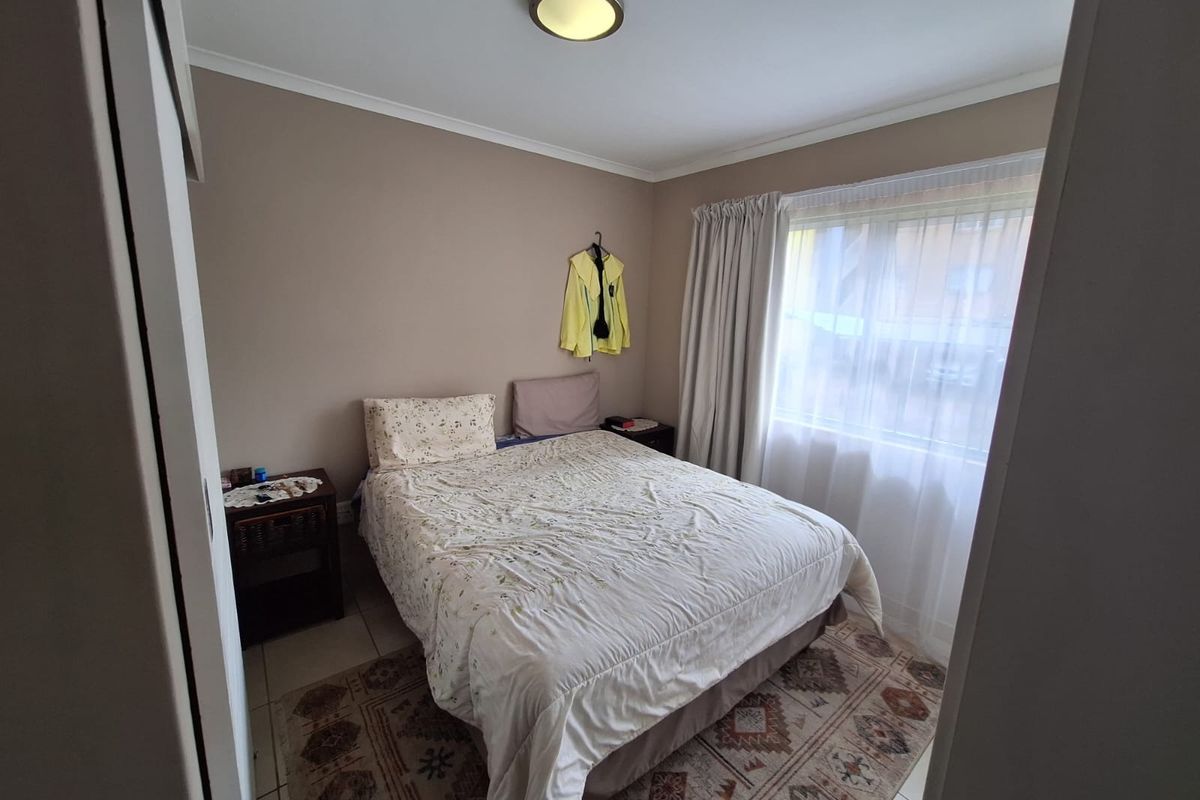 A functional bedroom featuring tiled flooring, a built-in cupboard, and a large window allowing natural light into the space.