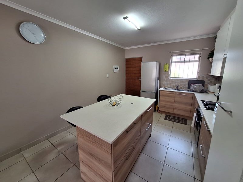 A functional kitchen featuring a central island, wood-finish cabinetry, tiled flooring, and integrated cooking appliances, providing a practical workspace.