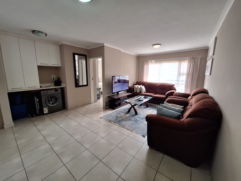 Open-plan living area featuring tiled flooring, built-in cabinetry with laundry appliance space, and natural light through large windows.
