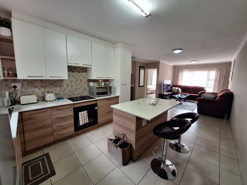 An open-plan living and kitchen area featuring modern two-tone cabinetry, a central kitchen island, and neutral tiled flooring throughout the space.