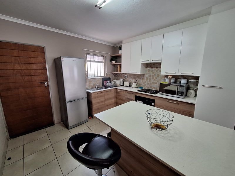 A functional kitchen featuring modern two-tone cabinetry, a central island with countertop seating, tiled backsplash, and integrated cooking appliances.