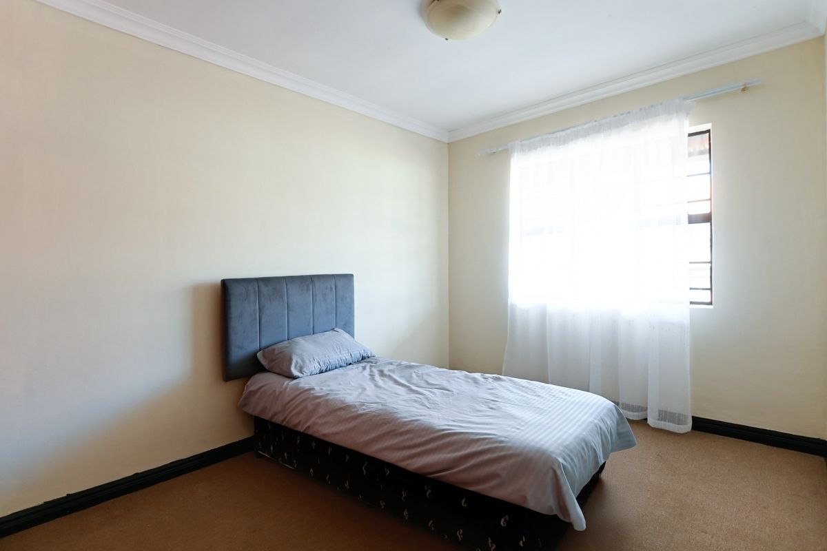 A simple bedroom featuring carpet flooring, coving, and a window fitted with security bars.