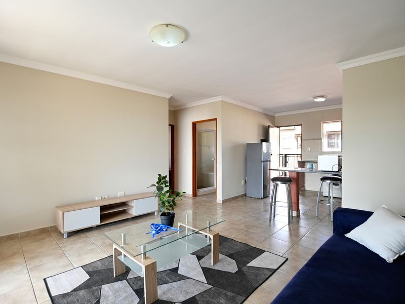 Open-plan living area featuring tiled flooring, a breakfast bar, and a functional kitchen layout with neutral wall finishes.