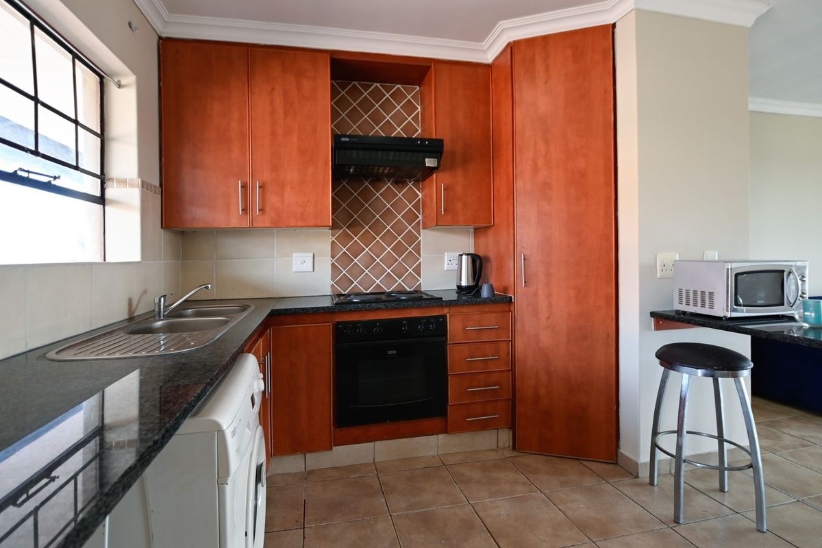 A functional kitchen featuring warm-toned wooden cabinetry, granite countertops, a built-in oven with hob, and tiled flooring.