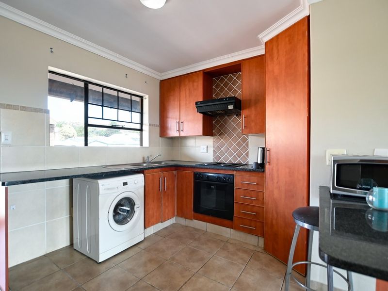 A functional kitchen featuring wood-finish cabinetry, dark countertops, built-in oven and hob, tiled backsplash, and space for a washing machine.