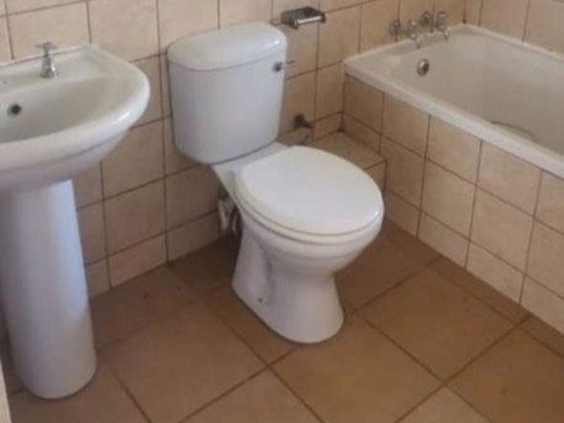 A functional bathroom featuring a pedestal basin, standard toilet, and a built-in bathtub with tiled wall and floor finishes.