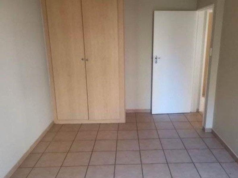 An empty bedroom featuring neutral tiled flooring and a built-in wooden wardrobe, providing a clean and versatile space.