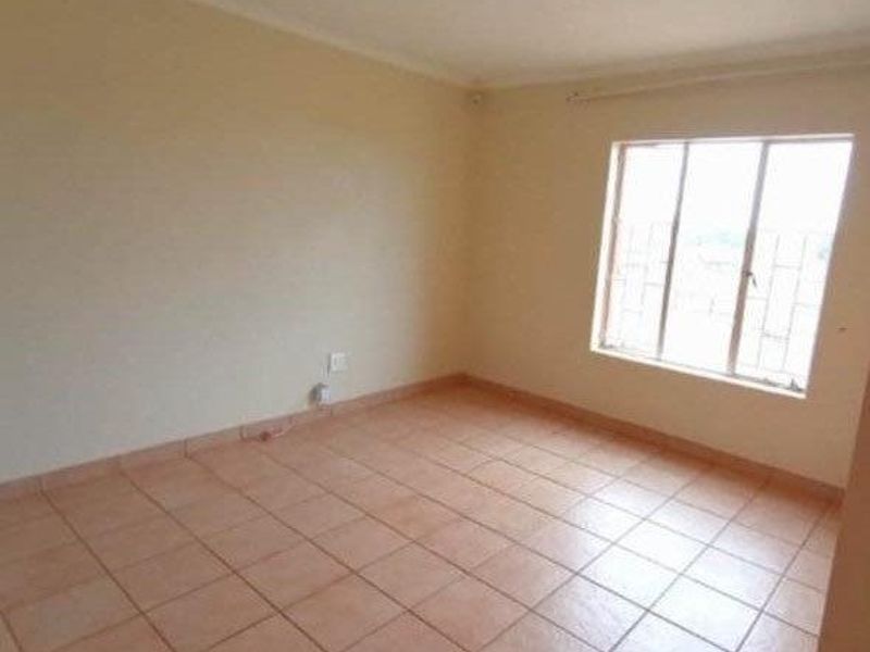 An empty bedroom featuring neutral walls, tiled flooring, and a window fitted with security bars.