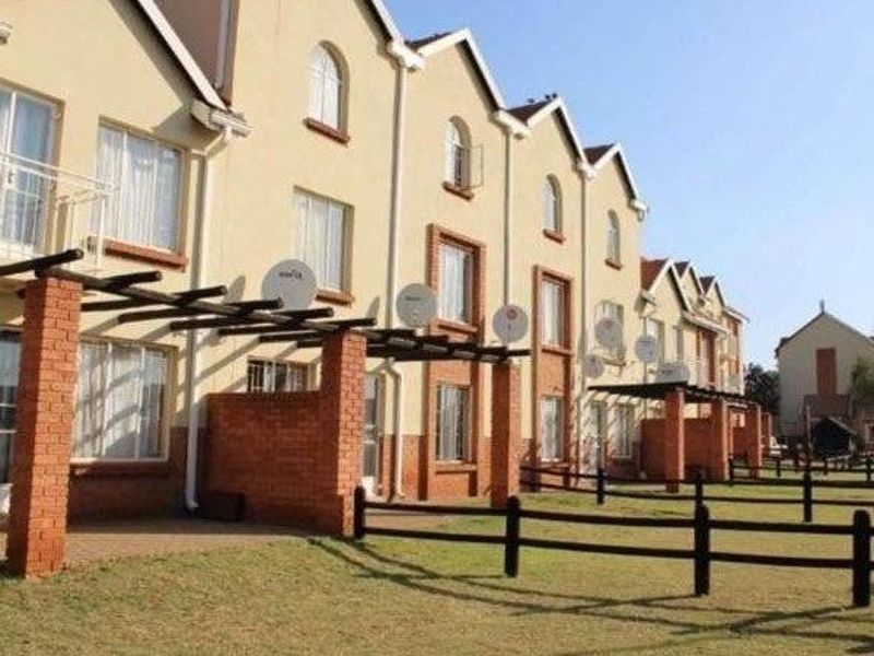 Rear elevation of a multi-unit apartment complex featuring brick pillars, timber pergolas, and shared garden space with post and rail fencing.
