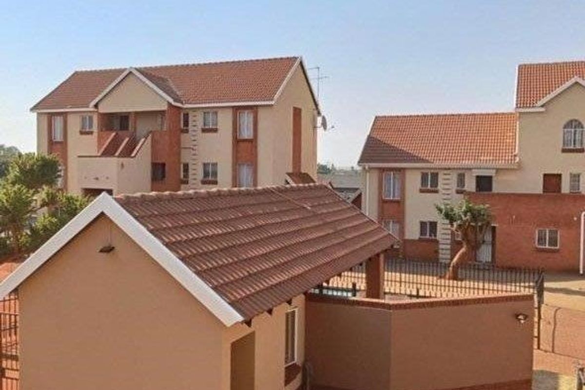 Exterior view of a residential apartment complex featuring multi-story buildings with tiled roofs and brick accents, set within a paved courtyard area.