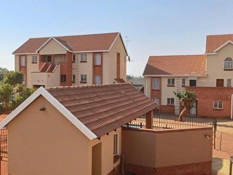 Exterior view of a residential apartment complex featuring multi-story buildings with tiled roofs and brick accents, set within a paved courtyard area.