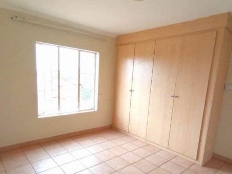 A bright, empty bedroom featuring tiled flooring, a large window with security bars, and ample built-in cupboard storage.