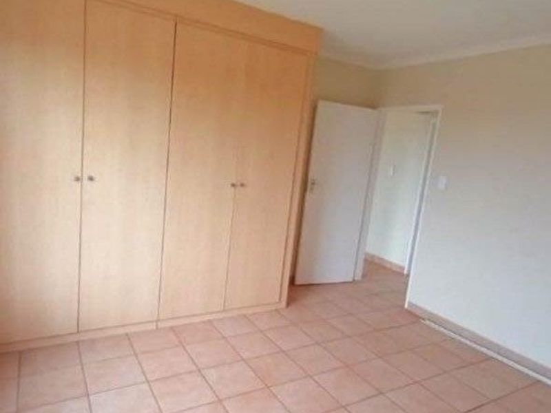 A vacant bedroom featuring built-in wooden cupboards and neutral tiled flooring, offering a clean and functional space ready for personalization.