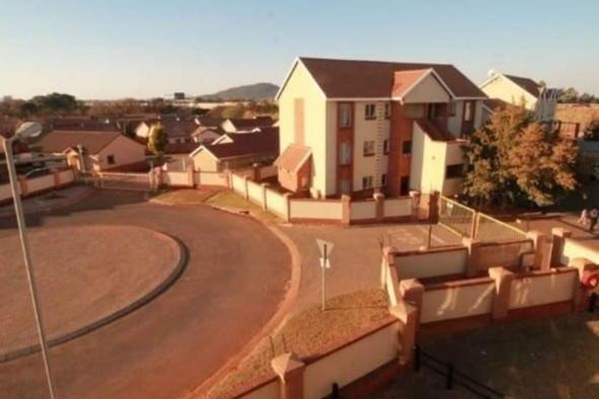 An aerial view of an apartment complex featuring a paved driveway, perimeter walling, and gated access within a residential estate.