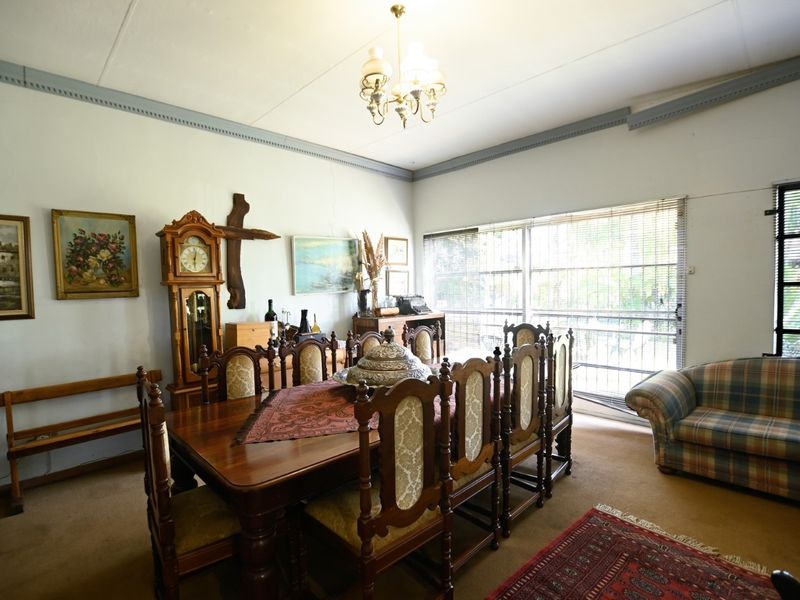 Spacious dining room featuring large windows with security bars, crown molding, and a central light fixture, offering a traditional layout ready for modernization.