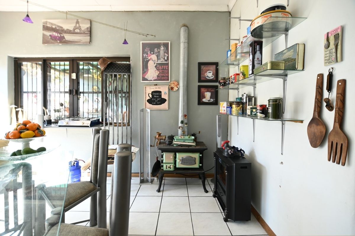 A kitchen area featuring tiled flooring, glass wall shelving, and a vintage-style cast iron stove, with security bars on the window.