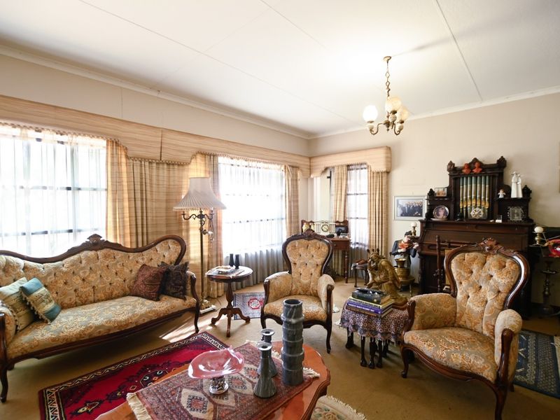 A traditional living room featuring classic ceiling cornices, decorative pelmets, and a central chandelier, offering a dated but well-maintained interior space.