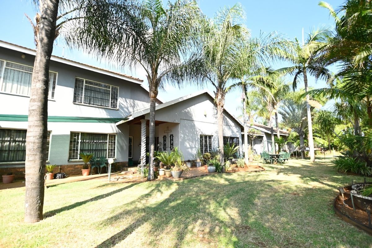 Rear view of the house featuring a paved patio area, established palm trees, and a well-maintained garden lawn.
