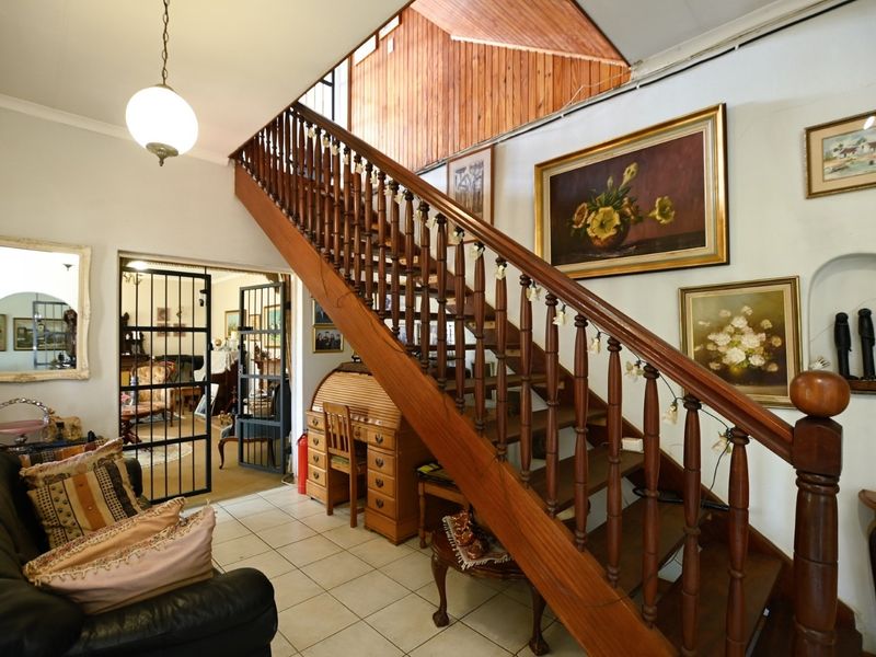 Spacious entrance hall featuring a prominent wooden staircase with traditional balustrade, tiled flooring, and access to adjacent living areas through a security gate.