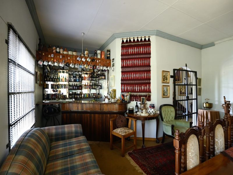 A dedicated home bar area featuring a built-in wooden counter, mirrored shelving, and a security gate leading to adjacent living spaces.