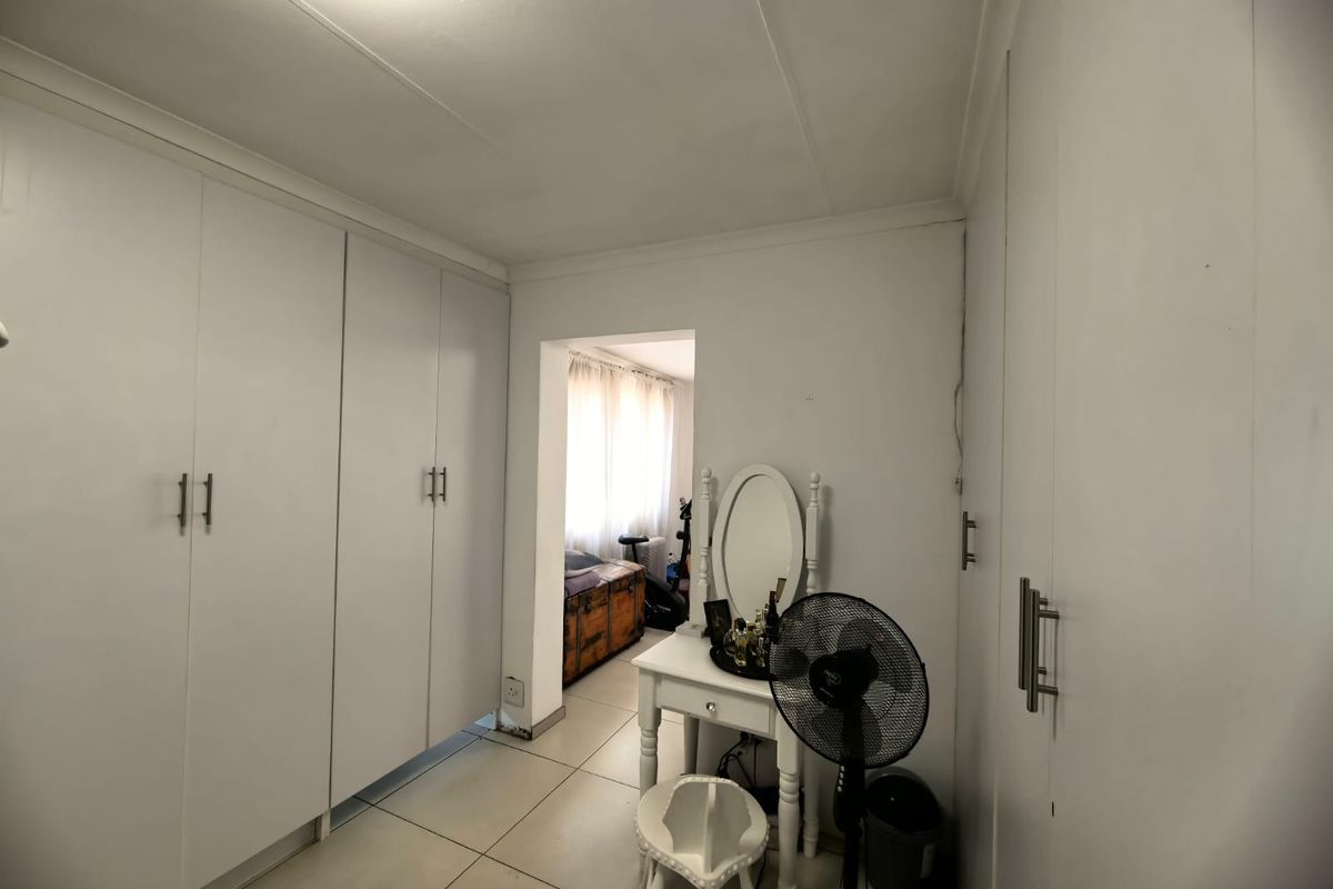 A bedroom featuring extensive built-in cupboards, neutral tiled flooring, and a doorway leading to an adjacent space.