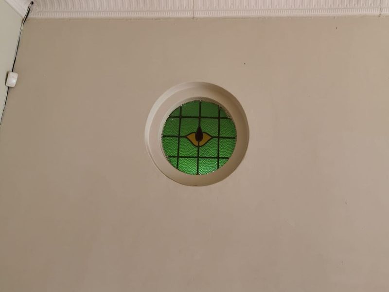A close-up view of a decorative circular stained glass window set into a wall with traditional ceiling cornice detailing.