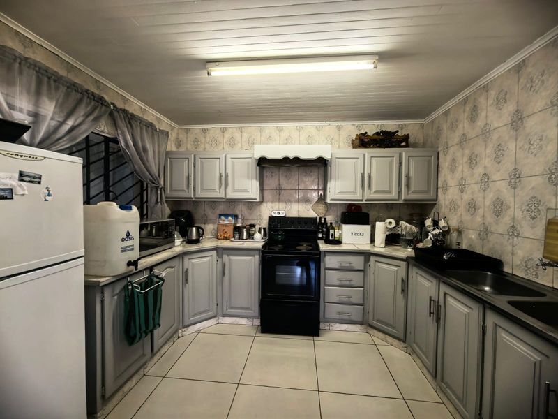 A functional kitchen featuring grey built-in cabinetry, a freestanding stove, double sink, and tiled finishes throughout.