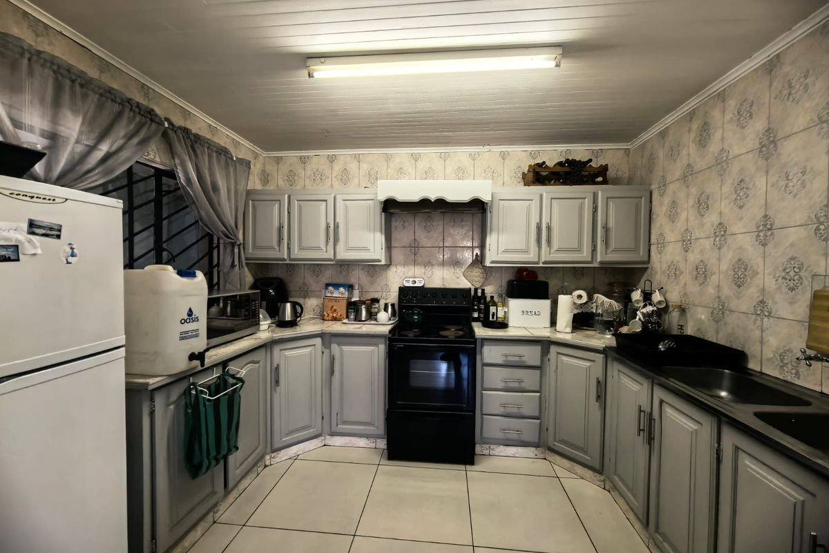 A functional kitchen featuring grey built-in cabinetry, a freestanding stove, double sink, and tiled finishes throughout.