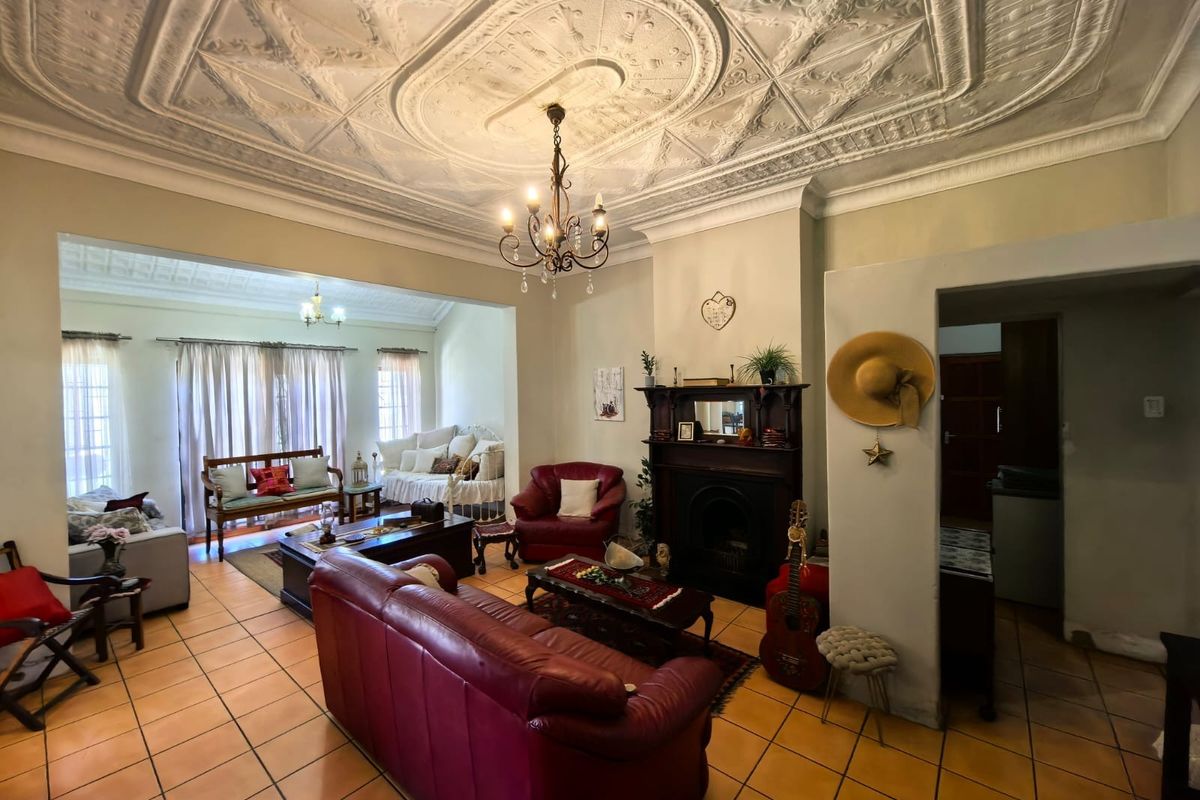 Spacious living room featuring a classic ornate pressed metal ceiling, tiled flooring, and a traditional fireplace with a timber mantelpiece.