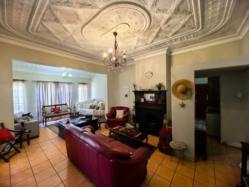 Spacious living room featuring a classic ornate pressed metal ceiling, tiled flooring, and a traditional fireplace with a timber mantelpiece.