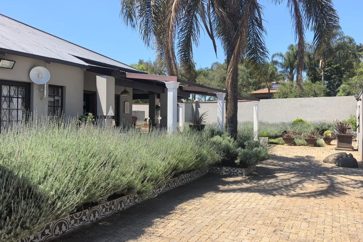 Rear exterior view featuring a covered patio with classical columns, decorative tiled planter boxes, and a paved courtyard area.