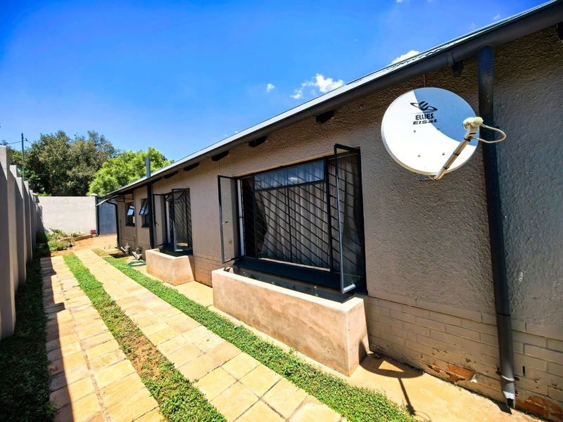 Rear exterior view of the house featuring a paved walkway, security bars on windows, and a mounted satellite dish.