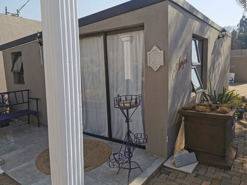 A view of a modern exterior structure featuring a tiled patio area, sliding glass doors, and top-hung windows, set against a paved outdoor space.