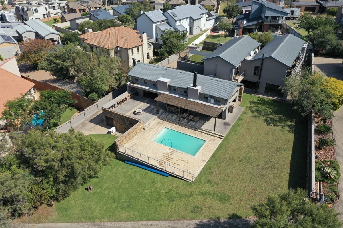 Aerial view of a modern residential property featuring a swimming pool, spacious lawn, and a covered patio area with a stone feature wall.