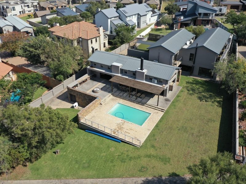 Aerial view of a modern residential property featuring a swimming pool, spacious lawn, and a covered patio area with a stone feature wall.