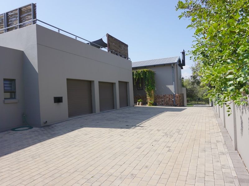 A modern exterior view featuring a triple garage, paved driveway, and a rooftop terrace with stone cladding accents.