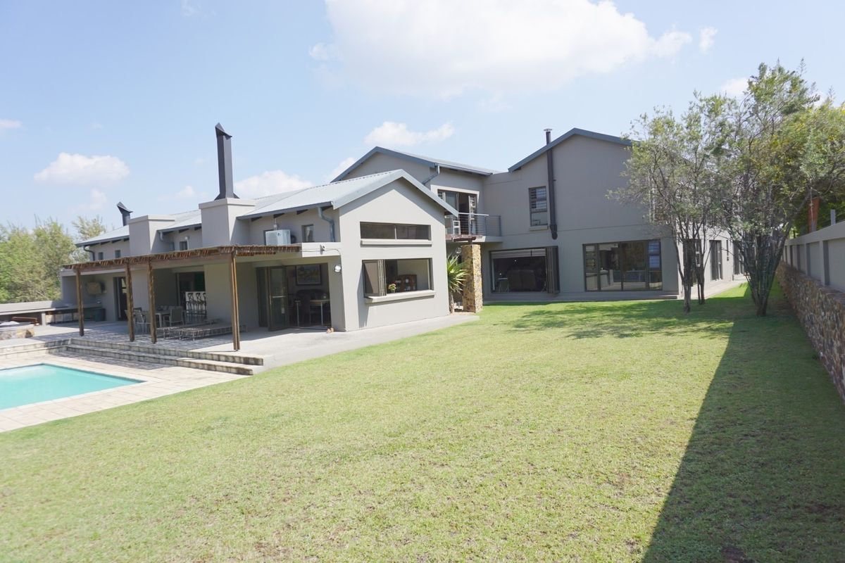 Spacious rear exterior view featuring a well-maintained lawn, swimming pool, and a covered patio area with a timber pergola and external fireplace.