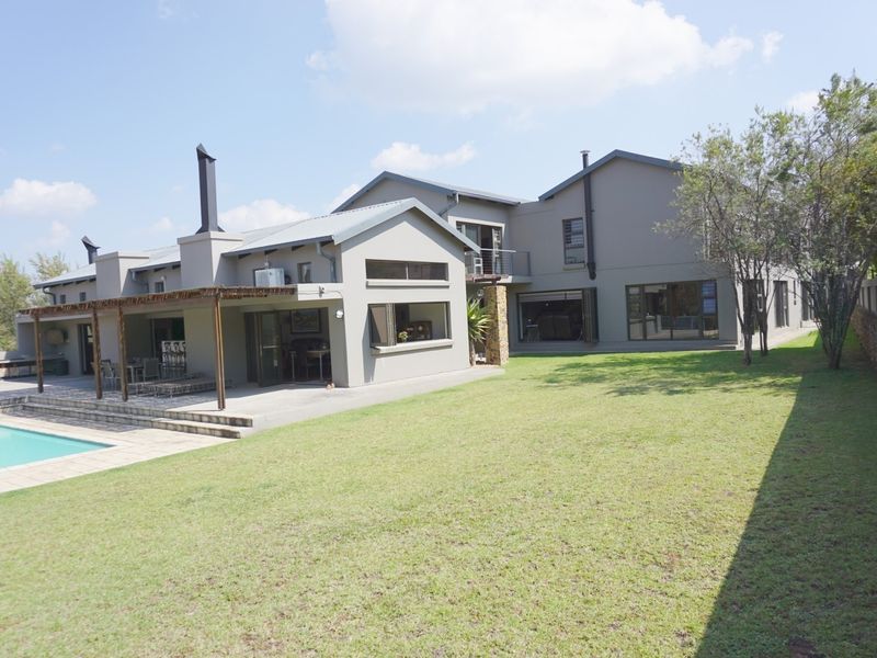 Spacious rear exterior view featuring a well-maintained lawn, swimming pool, and a covered patio area with a timber pergola and external fireplace.