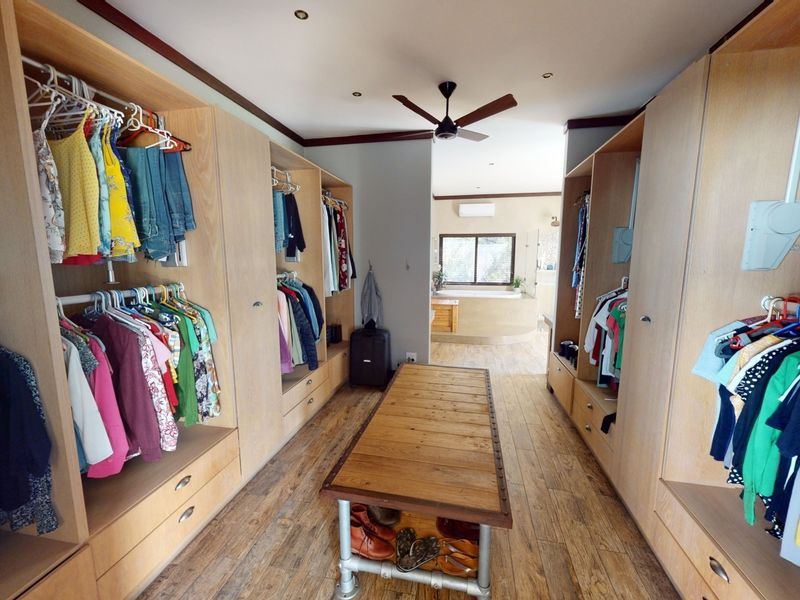 A spacious walk-in closet featuring extensive built-in wooden cabinetry, laminate flooring, and a ceiling fan, with an open transition to the adjoining bathroom area.