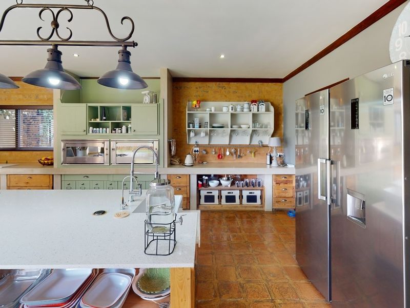 Spacious kitchen featuring a large island, built-in appliances, exposed brick walls, and terracotta flooring, offering a warm and functional culinary space.