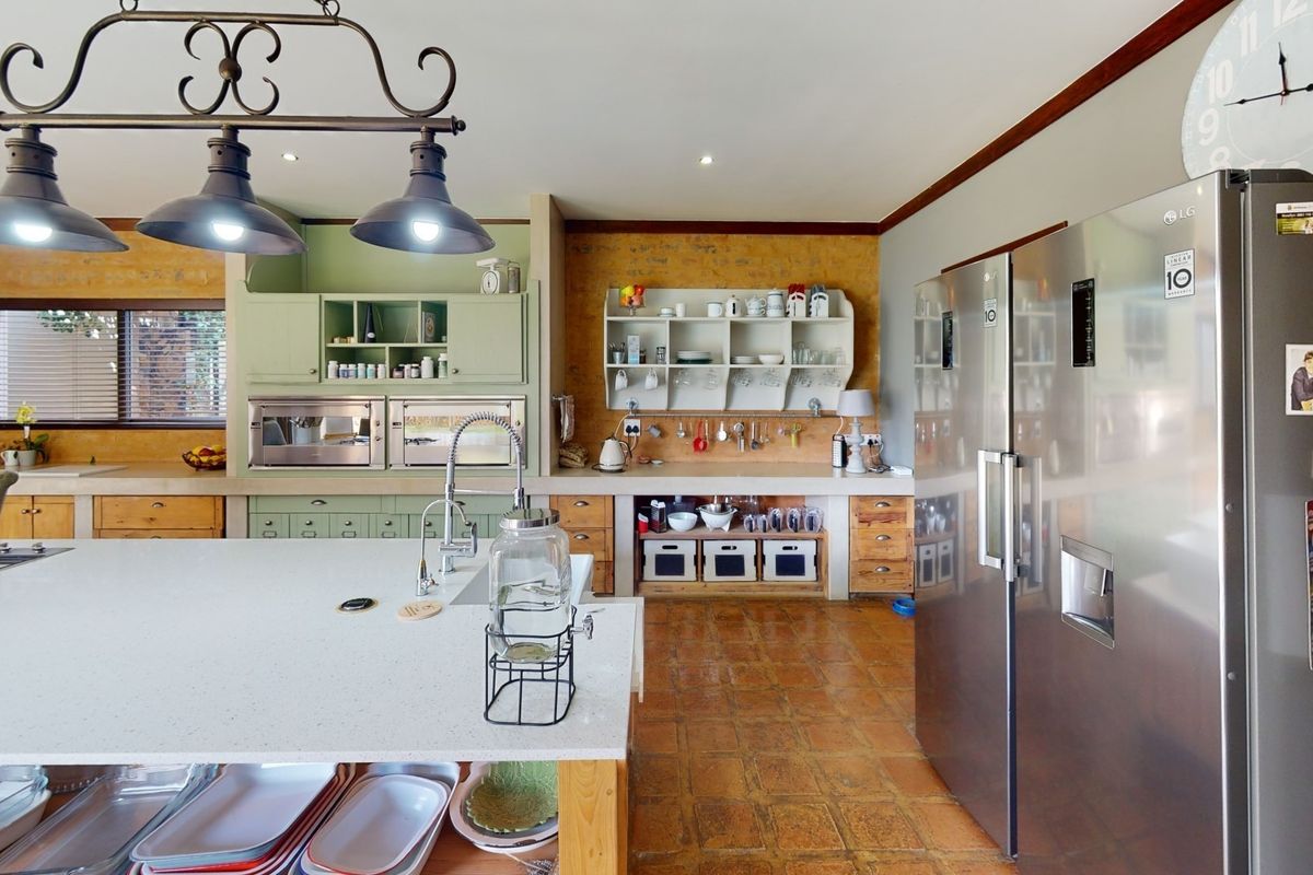 Spacious kitchen featuring a large island, built-in appliances, exposed brick walls, and terracotta flooring, offering a warm and functional culinary space.