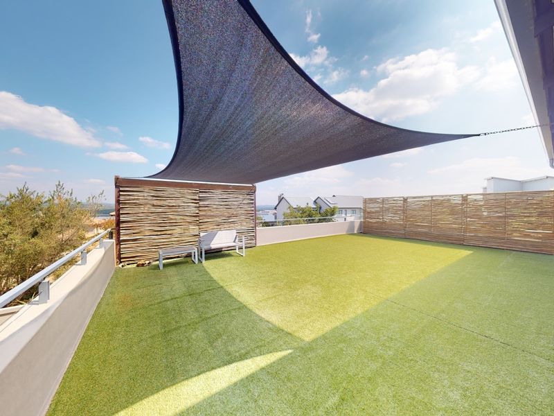 Spacious outdoor balcony featuring artificial turf, a protective shade sail, and bamboo privacy screening, offering a versatile area for relaxation.