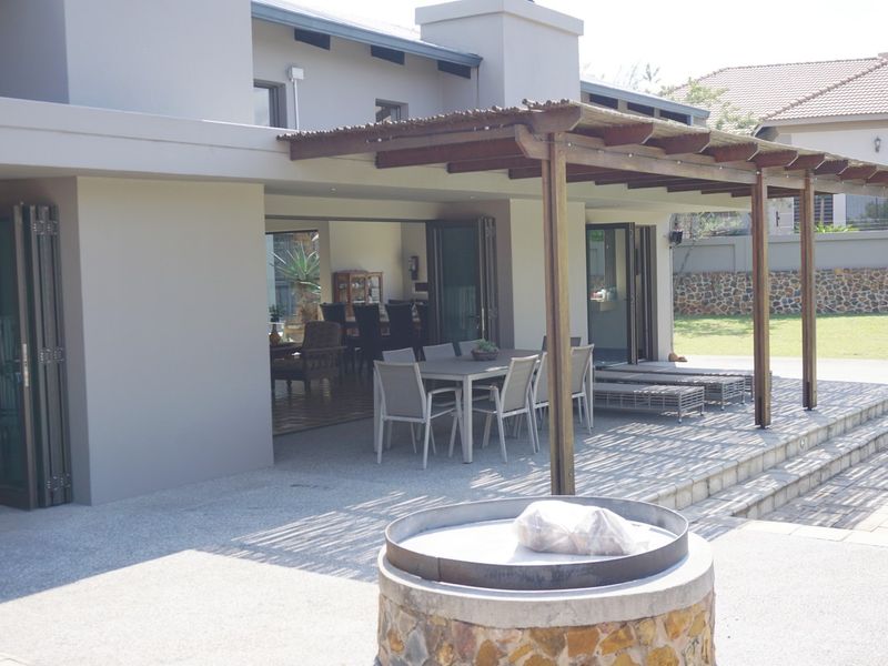 Spacious covered patio featuring a timber pergola, built-in braai, and seamless indoor-outdoor flow through large stacking doors onto the garden.