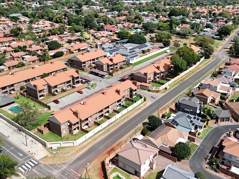 Aerial view of a residential apartment complex featuring multiple brick buildings, tiled roofs, communal parking, and a swimming pool within a suburban neighborhood.