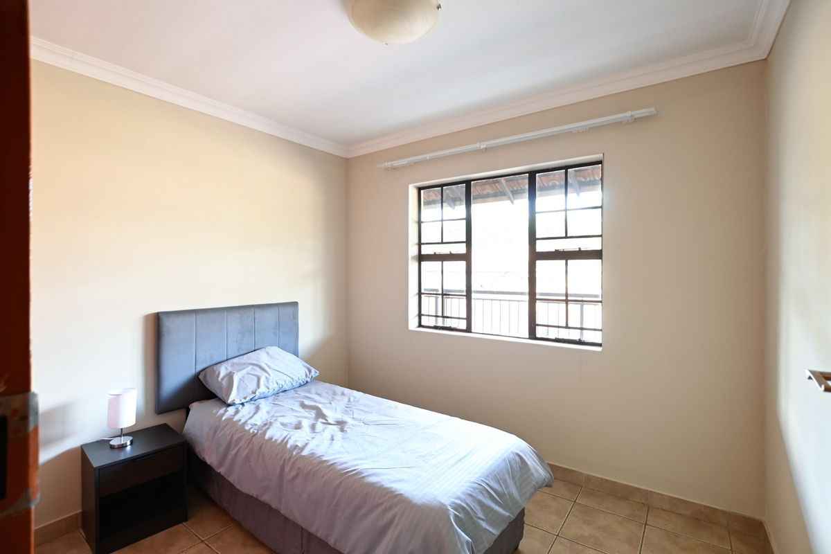 A functional bedroom featuring tiled flooring, coved ceilings, and a window fitted with security bars and a curtain rail.