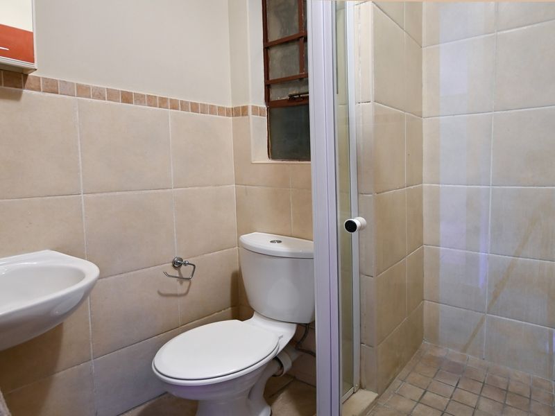 A functional bathroom featuring a wall-mounted basin, toilet, and a separate shower enclosure with tiled finishes.