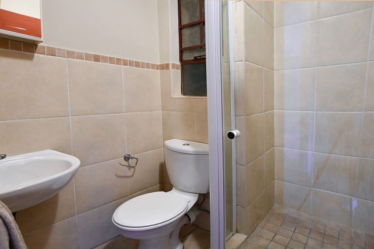 A functional bathroom featuring a wall-mounted basin, toilet, and a separate shower enclosure with tiled finishes.
