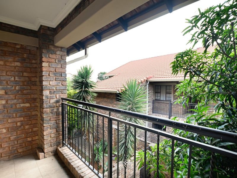 A covered balcony featuring exposed brickwork, a wrought iron balustrade, and tiled flooring, overlooking the complex garden area.