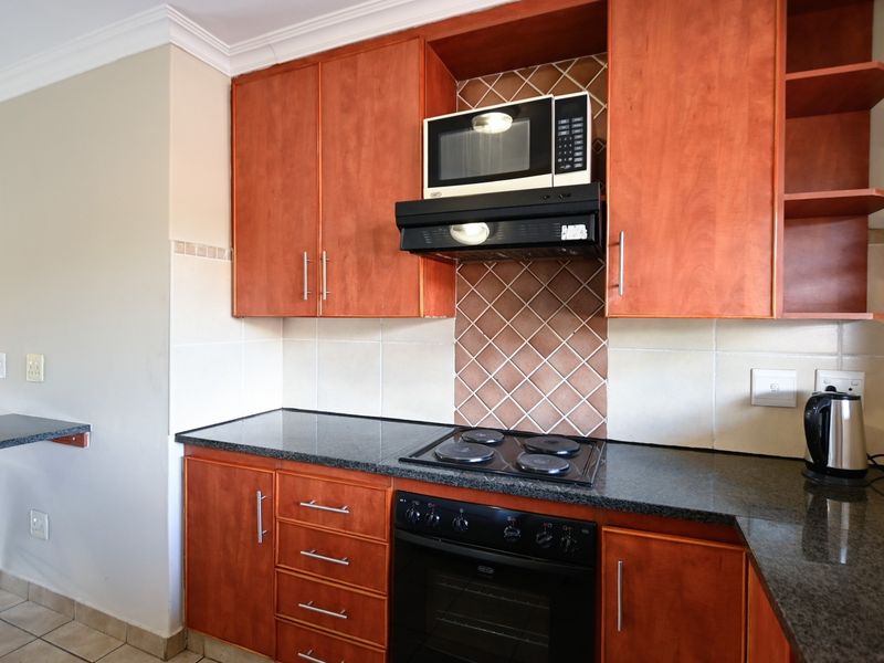 A functional kitchen featuring warm-toned wooden cabinetry, granite countertops, a built-in oven with hob, and a convenient breakfast bar extension.